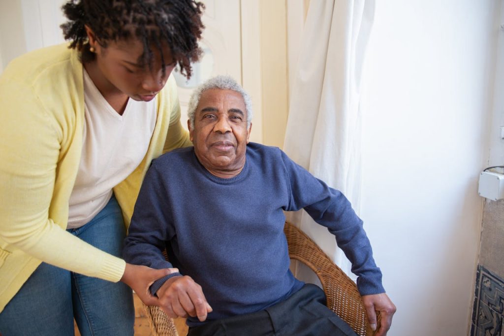 A woman assists an elderly man indoors, focusing on care and support.